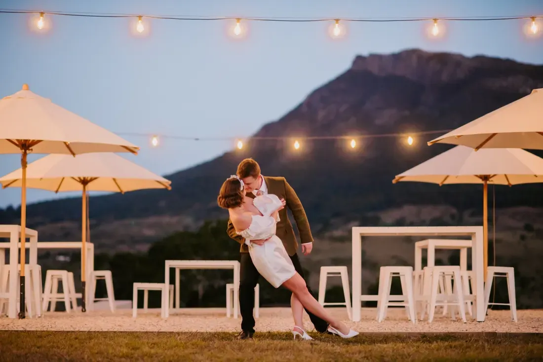 Bride and groom dancing at dusk among the umbrellas at Maroon Hill Estate, with mountains behind them
