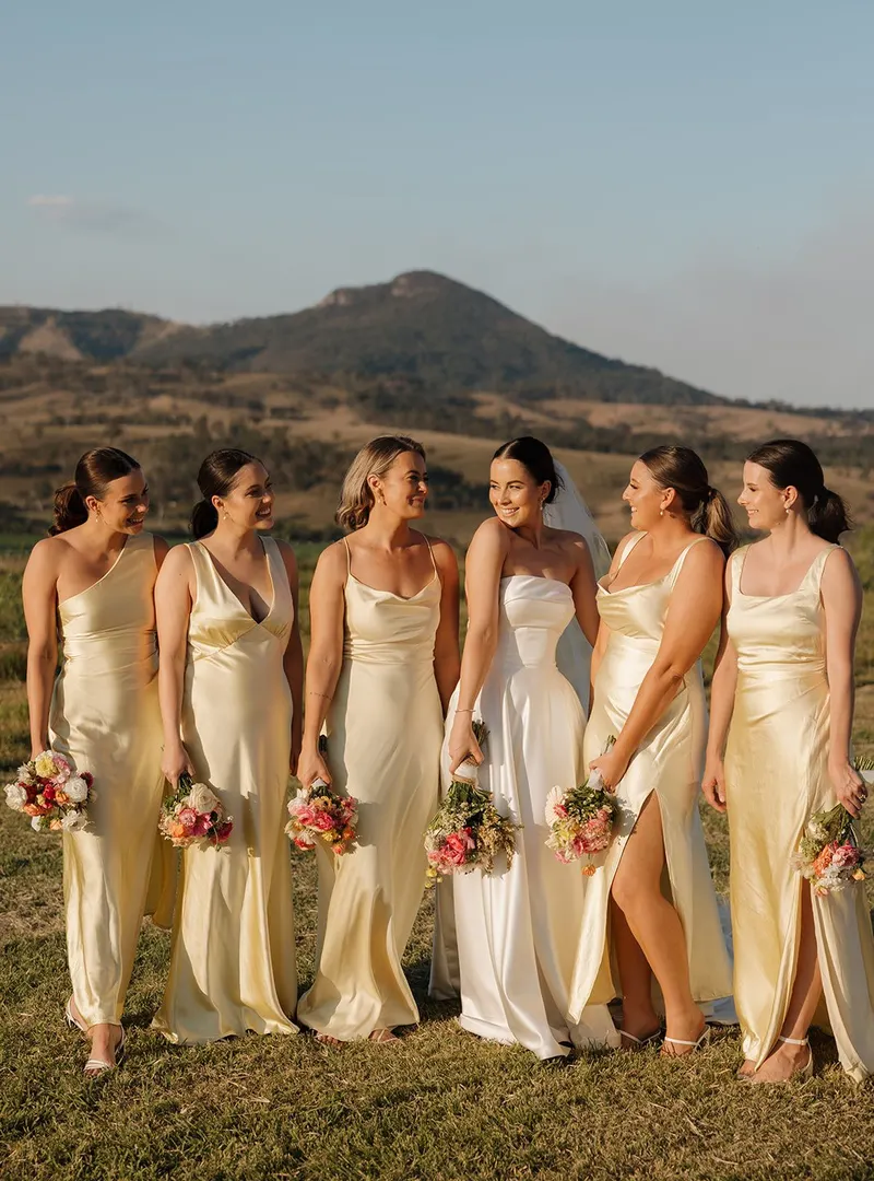 Bride with her bridesmaids in golden dresses, with Mount Maroon behind them at Maroon Hill Estate