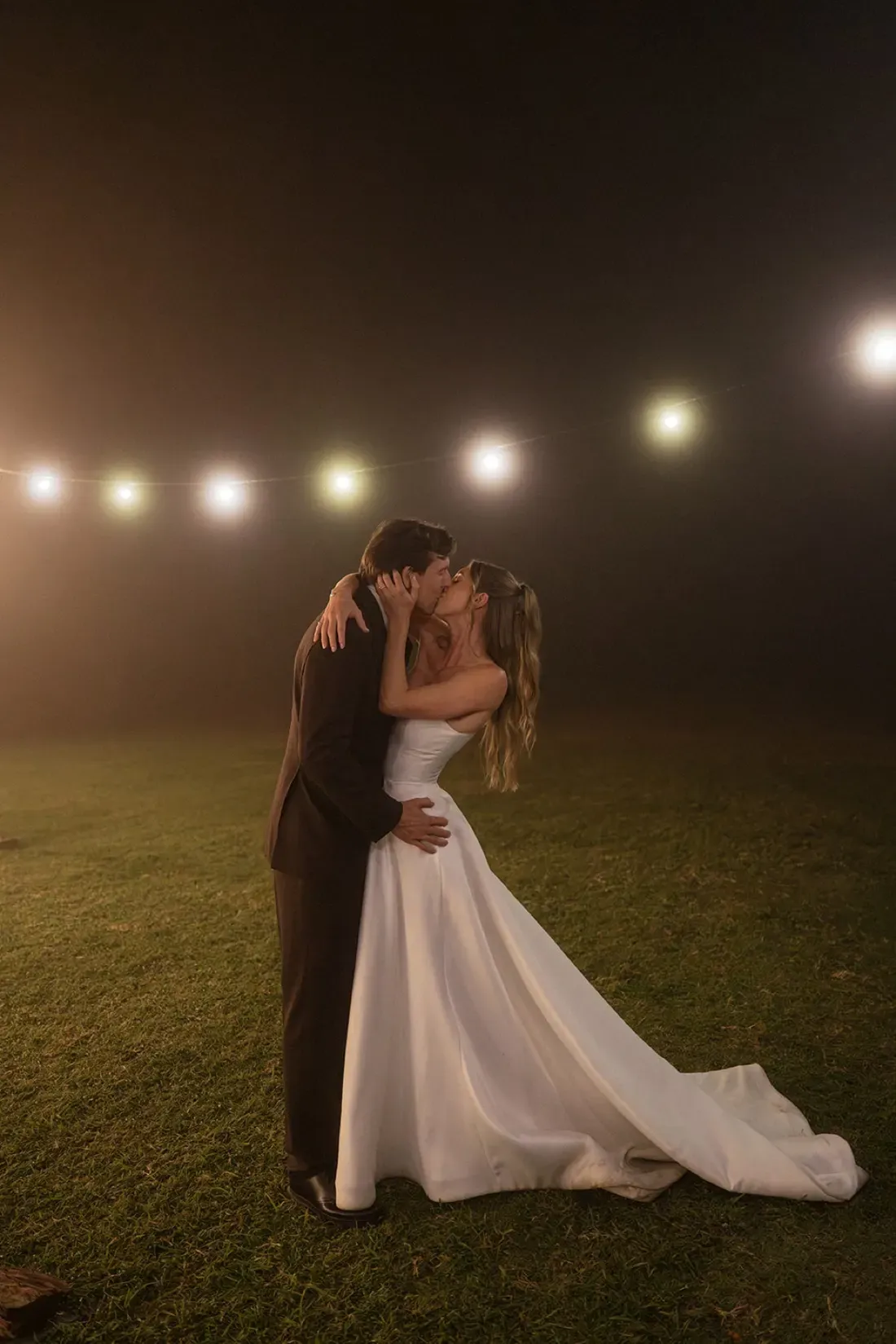 Bride and groom kissing under festoon lights in the fog at Maroon Hill Estate