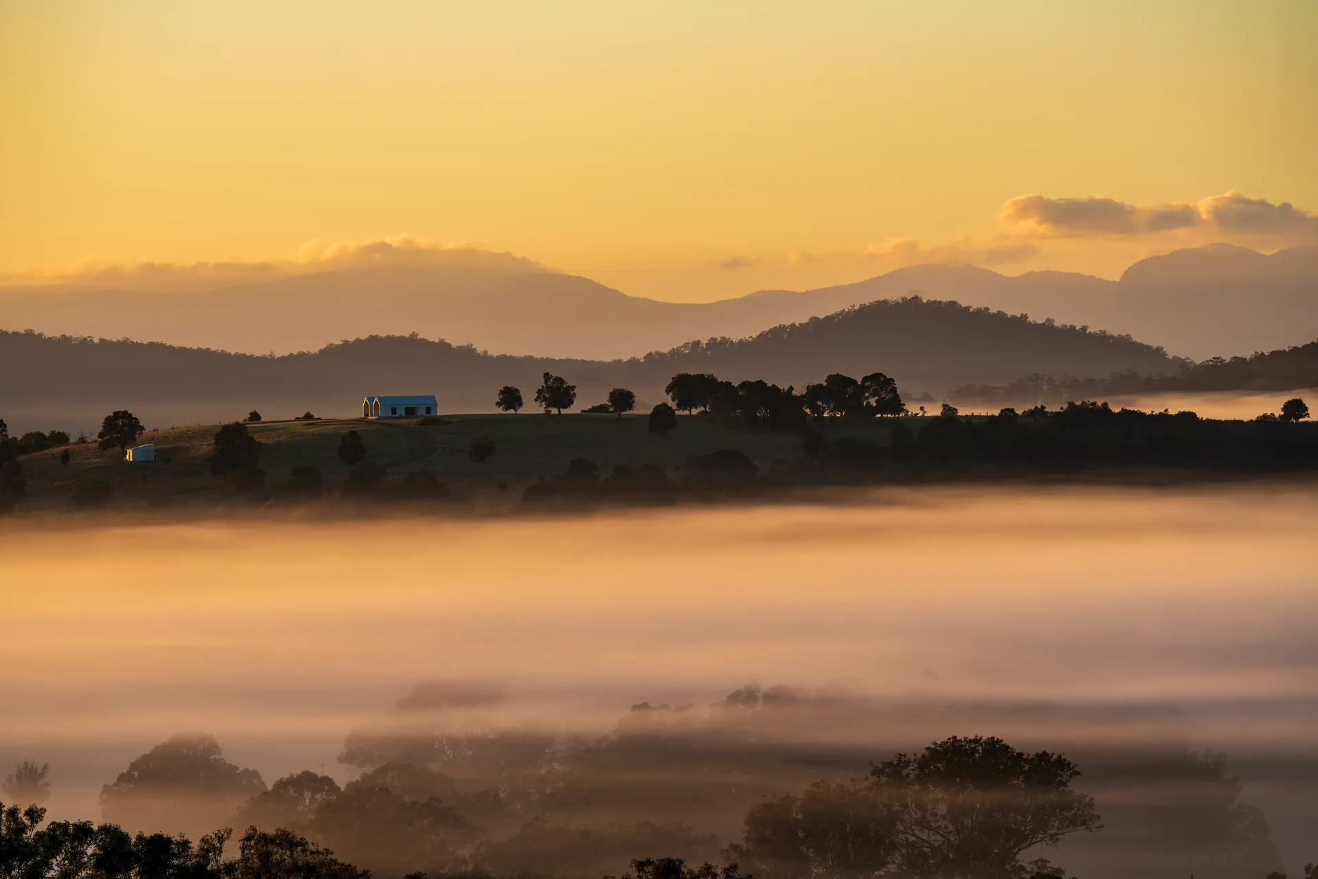 Maroon Hill Estate's gabled venue on the hilltop above a sea of fog at sunrise, with mountains in the distance