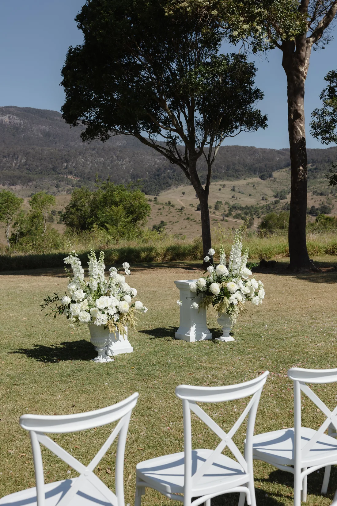 Ceremony florals in white urns beneath gum trees, mountain views behind