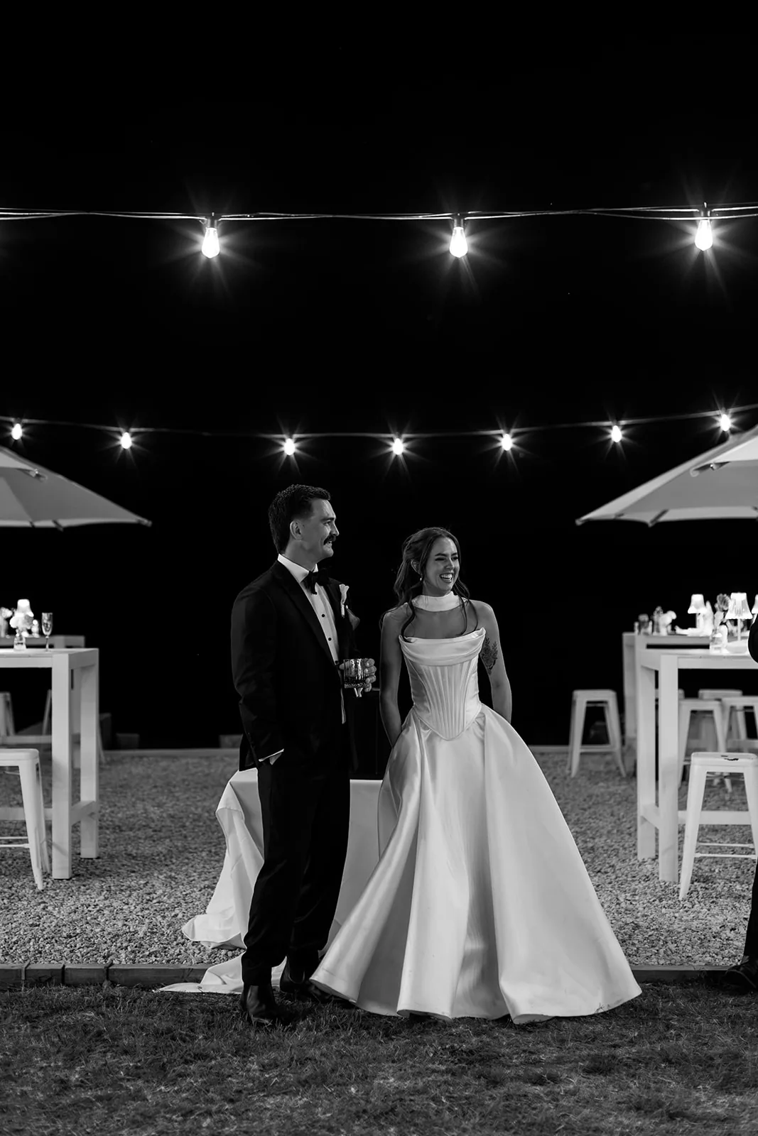 Black and white photo of Ally and Braydon laughing together under string lights at night
