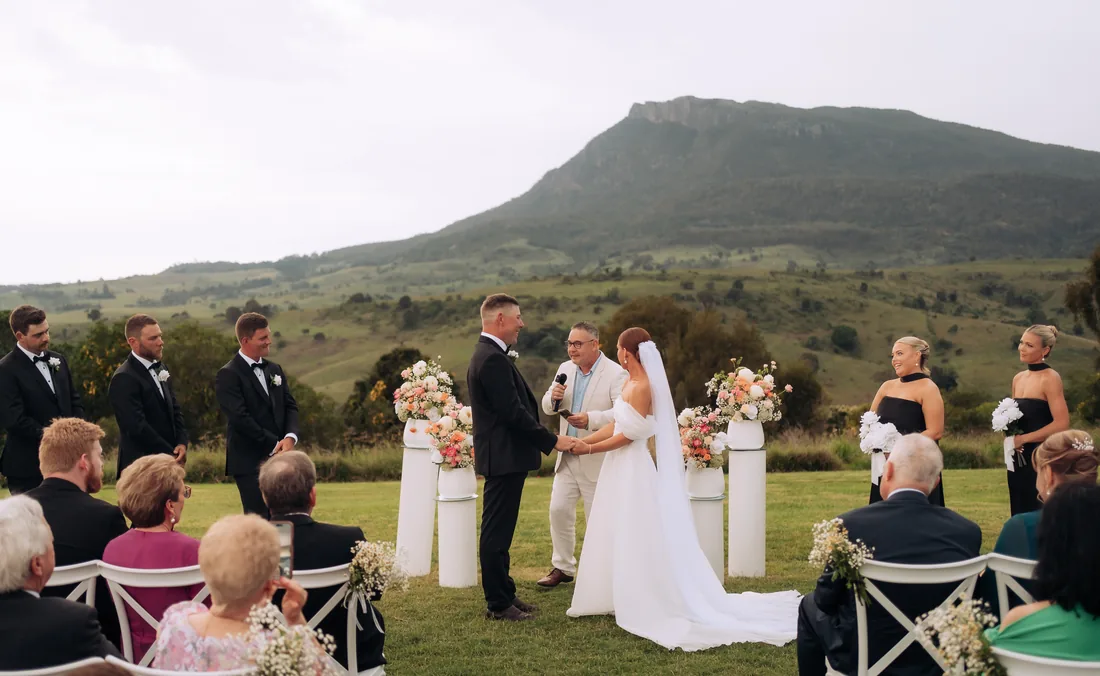 Deanna and Michael exchanging vows with the celebrant, mountain views behind