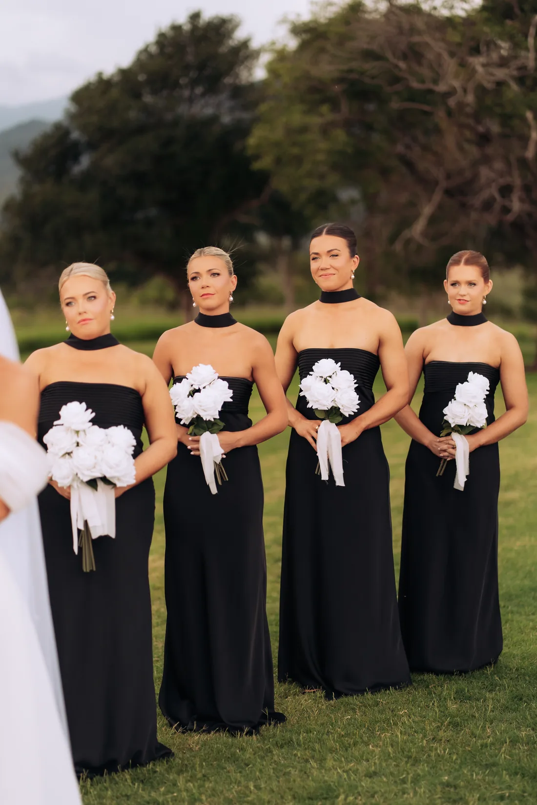 Four bridesmaids in black gowns holding white rose bouquets