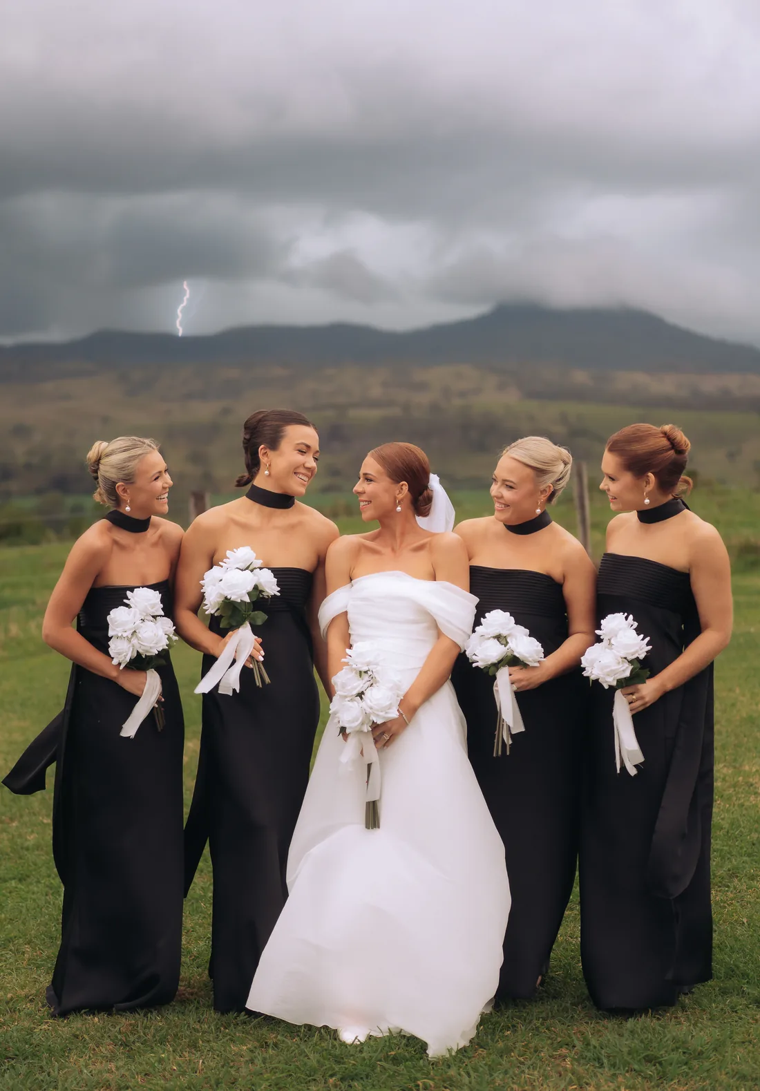 Bridesmaids and bride laughing together with lightning visible in the stormy sky behind