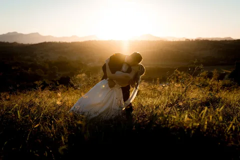 A couple kissing in the long grass as the sun sets behind the ranges