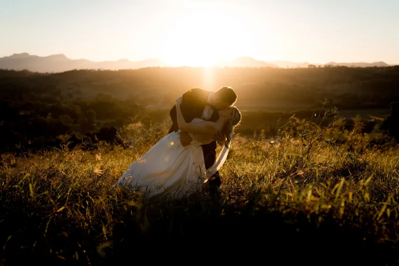 Gabi and Alec embracing in a sunlit field, backlit by the setting sun