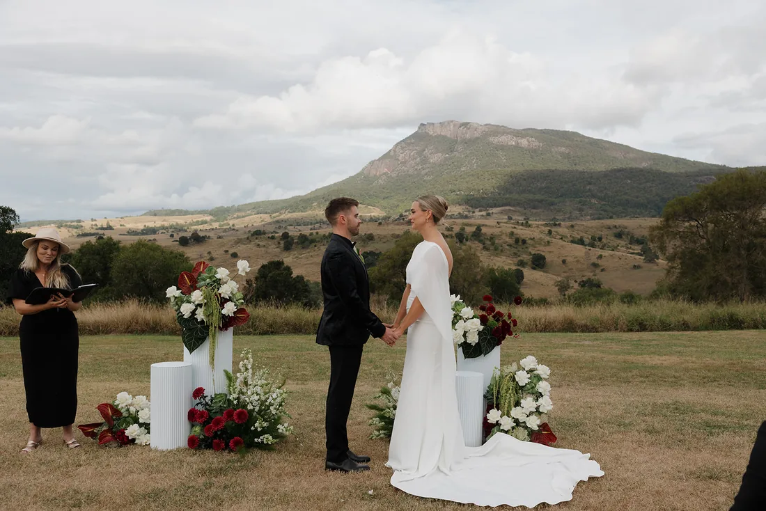 Jess and Cory exchanging vows, celebrant beside them, mountain views behind