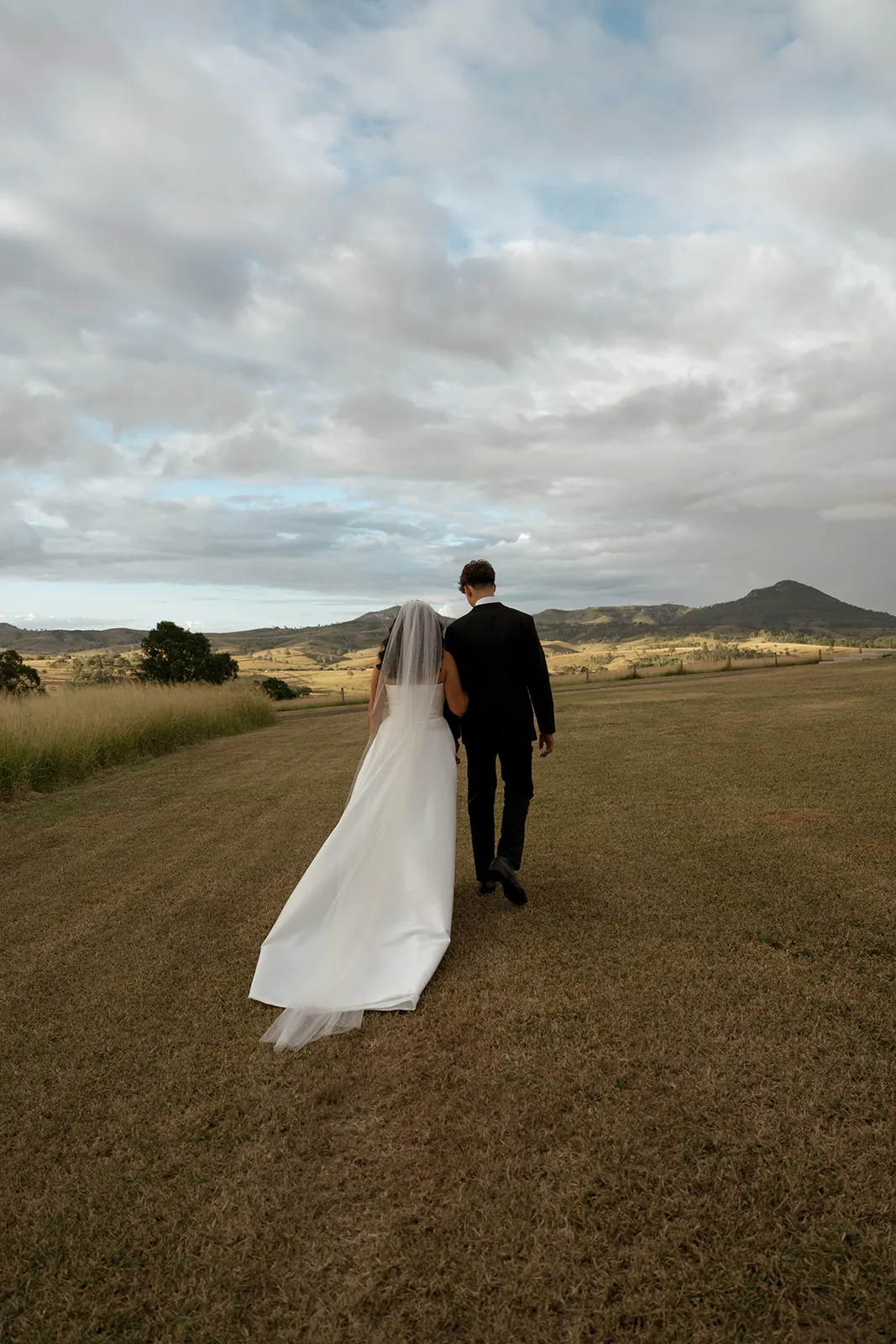 Jodi and Frank walking hand in hand across the paddock, back view
