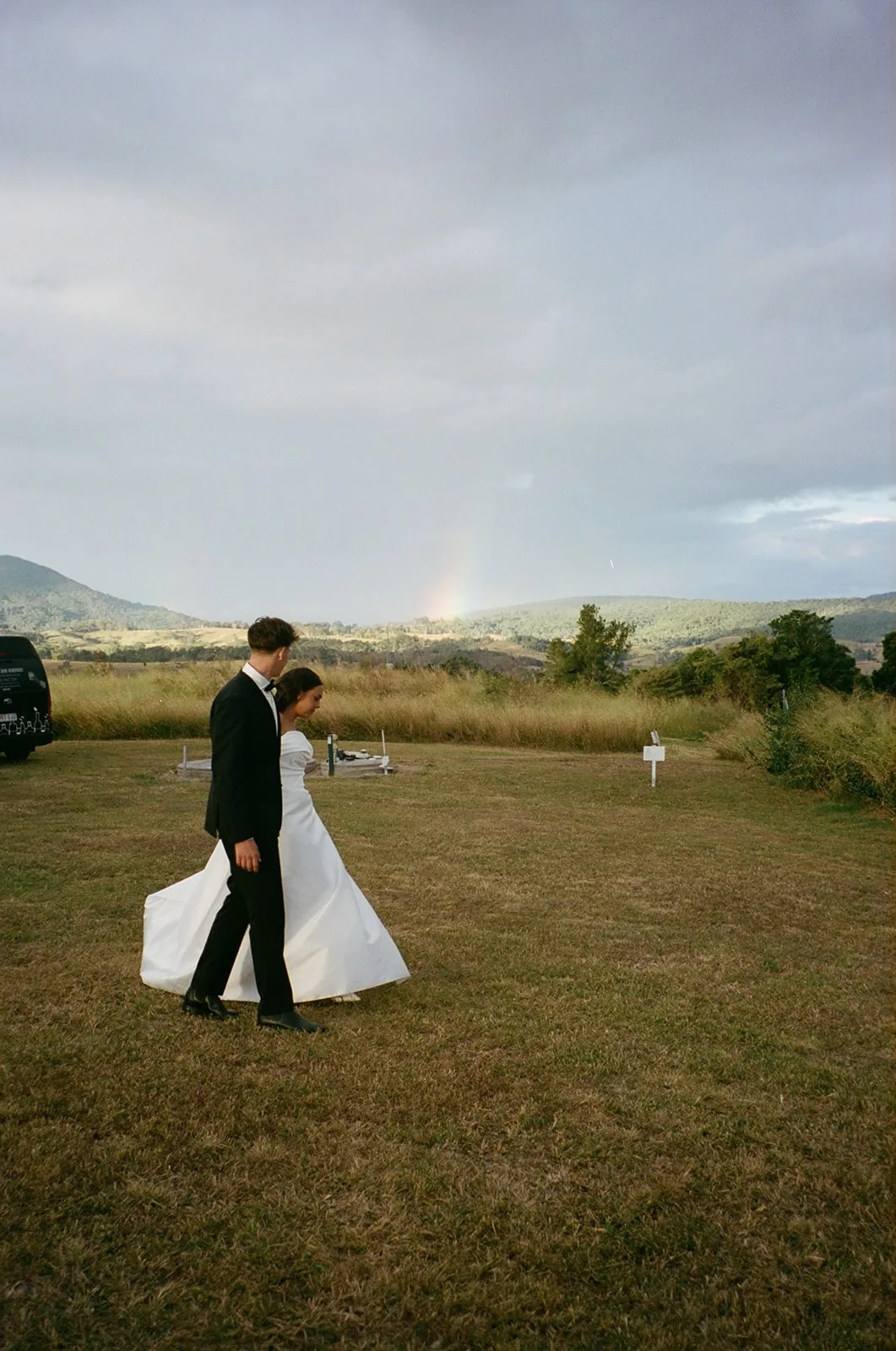 Jodi and Frank walking across the lawn with a rainbow visible over the hills