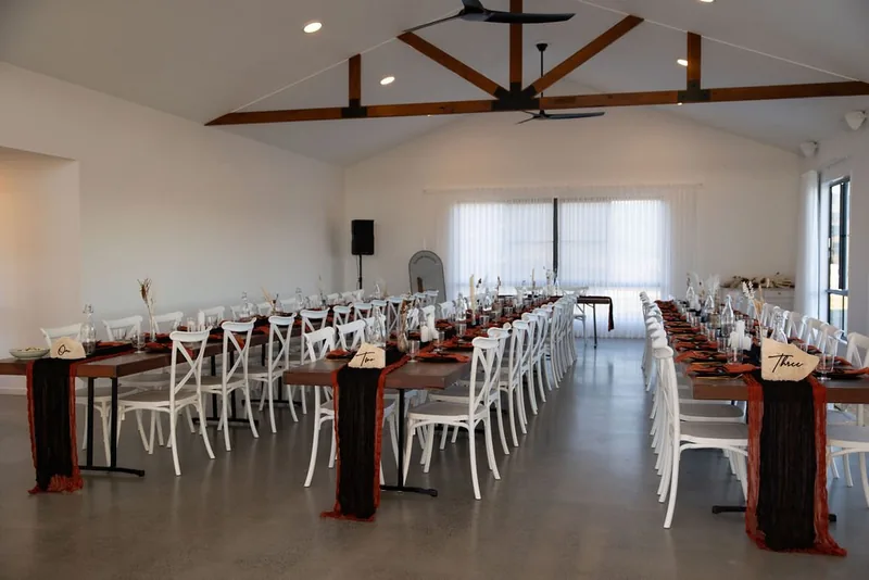 The reception room with the timber dining tables and white cross-back chairs set in long rows
