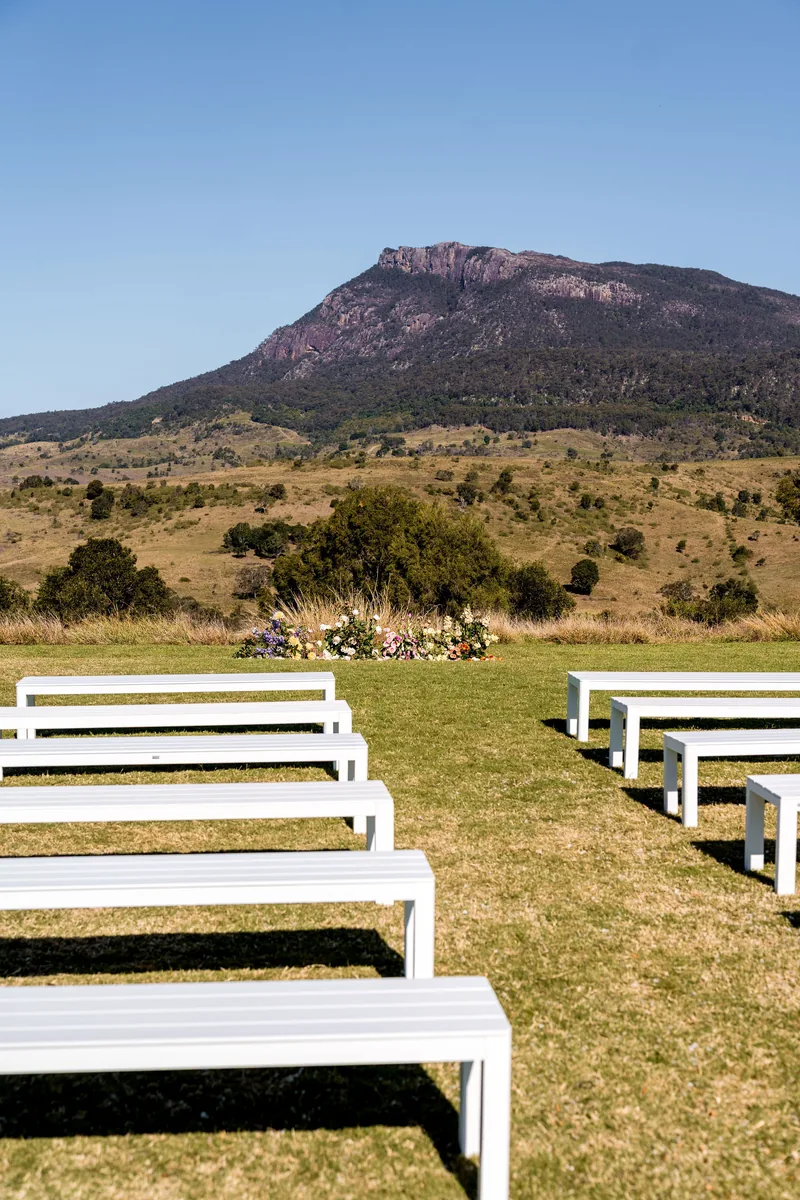 White bench seats lined up on the lawn under a blue sky, Mount Maroon behind