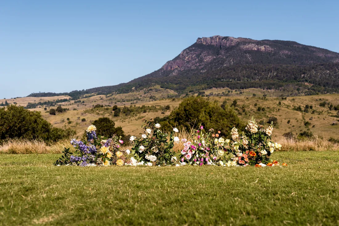 Colourful wildflower ceremony arrangement on the lawn, mountain backdrop