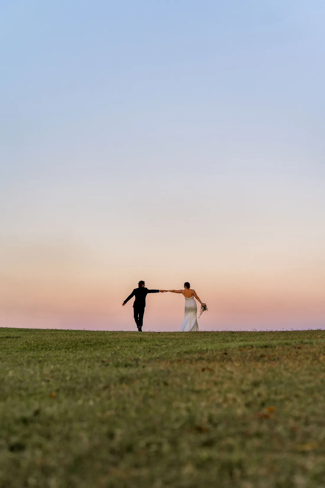 Kylee and Cameron holding hands and walking together at dusk, silhouetted against the sunset sky