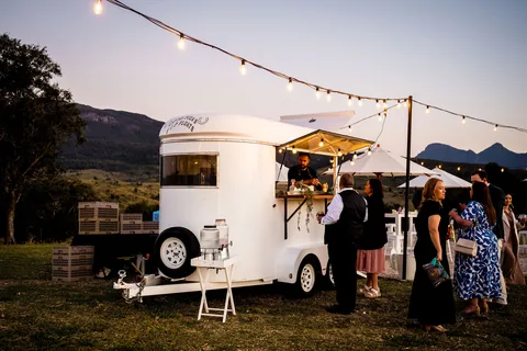 Guests at a horse float bar under festoon lights at dusk