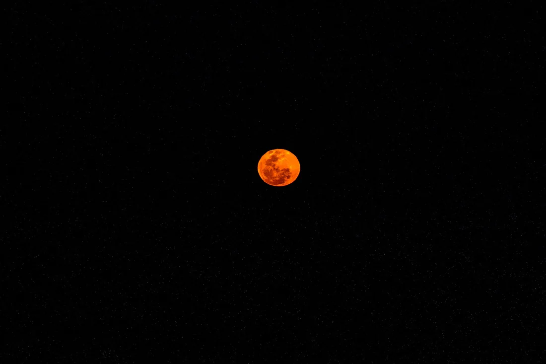 A full blood moon glowing orange in the night sky