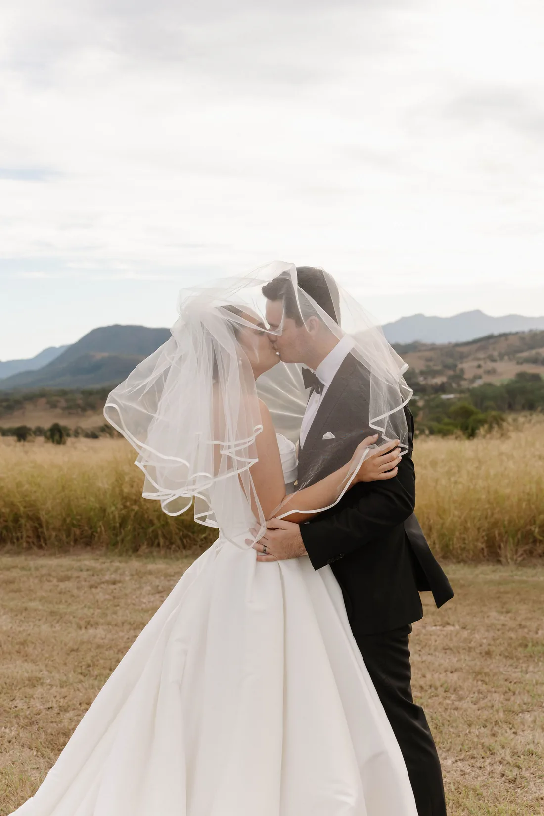 Laura and Connor kissing under her veil in a golden paddock