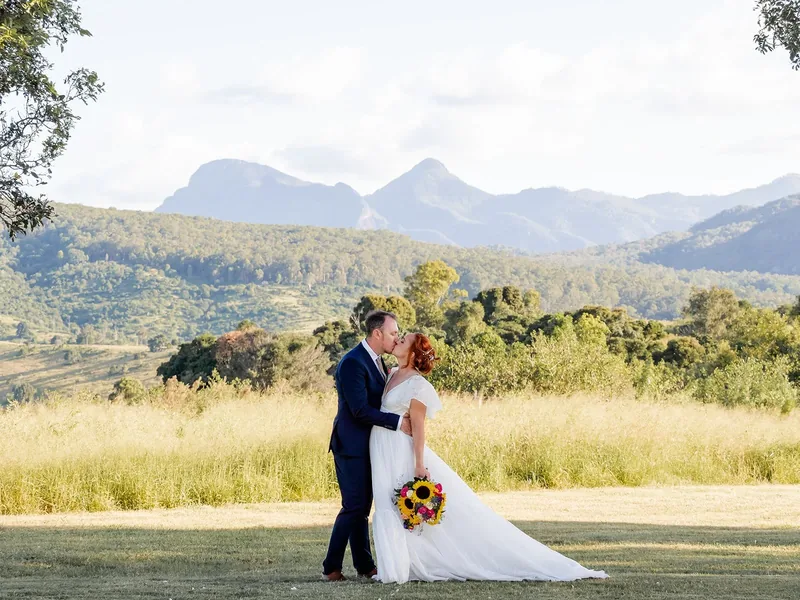 Leisa and Russell kissing in a grassy field with layered mountain views behind them