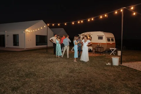 Guests beside a vintage caravan bar under festoon lights at night