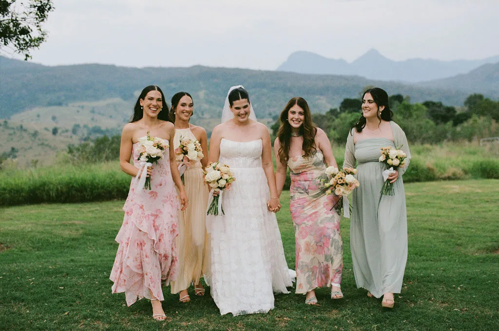 Bride walking with her four bridesmaids in mismatched floral and pastel dresses, mountains behind