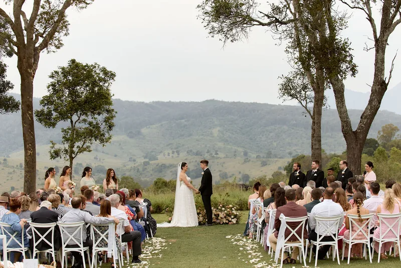 Guests seated on white cross-back chairs for a ceremony between the gum trees