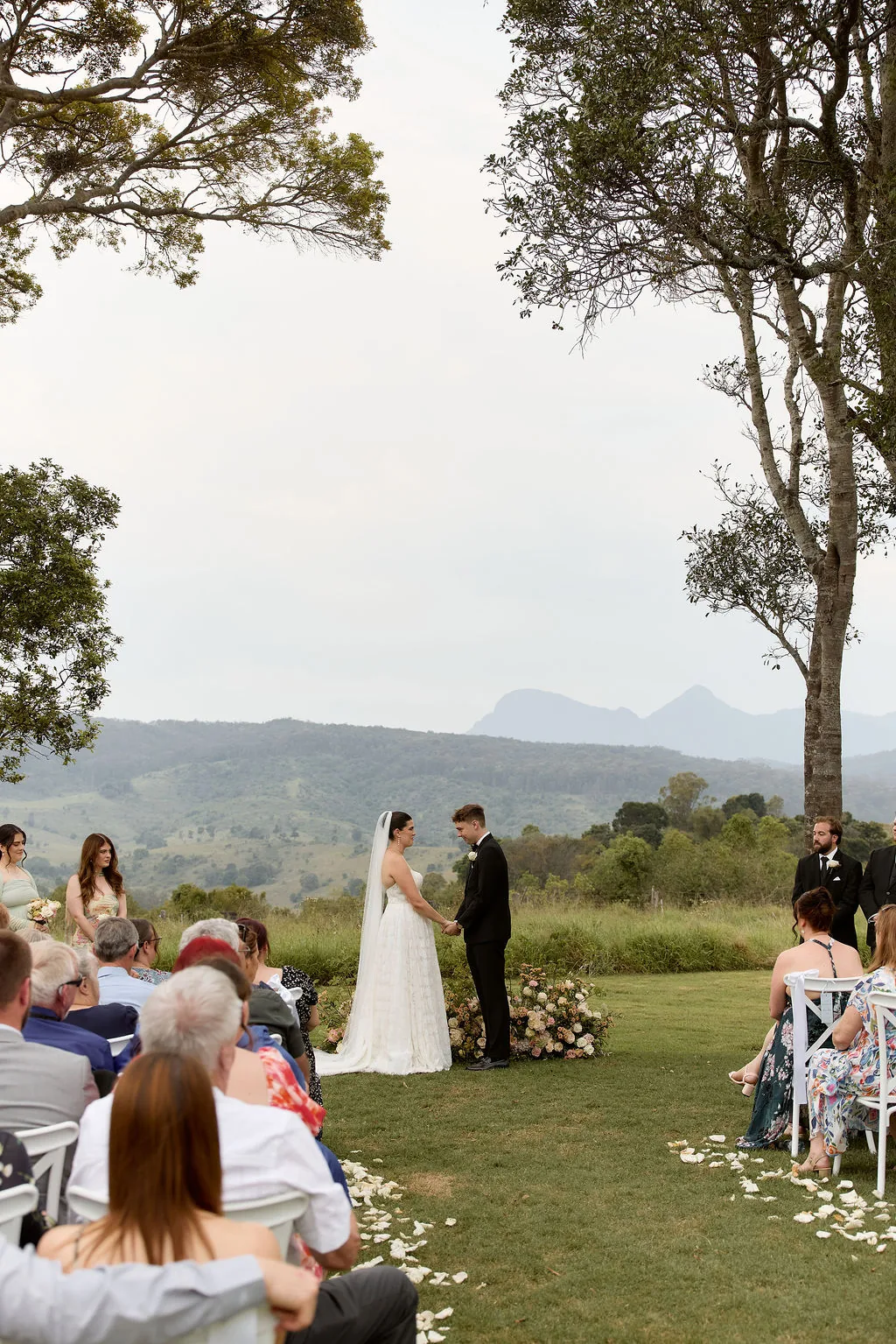 Rebecca and Benjamin exchanging vows, groomsmen and mountain views behind