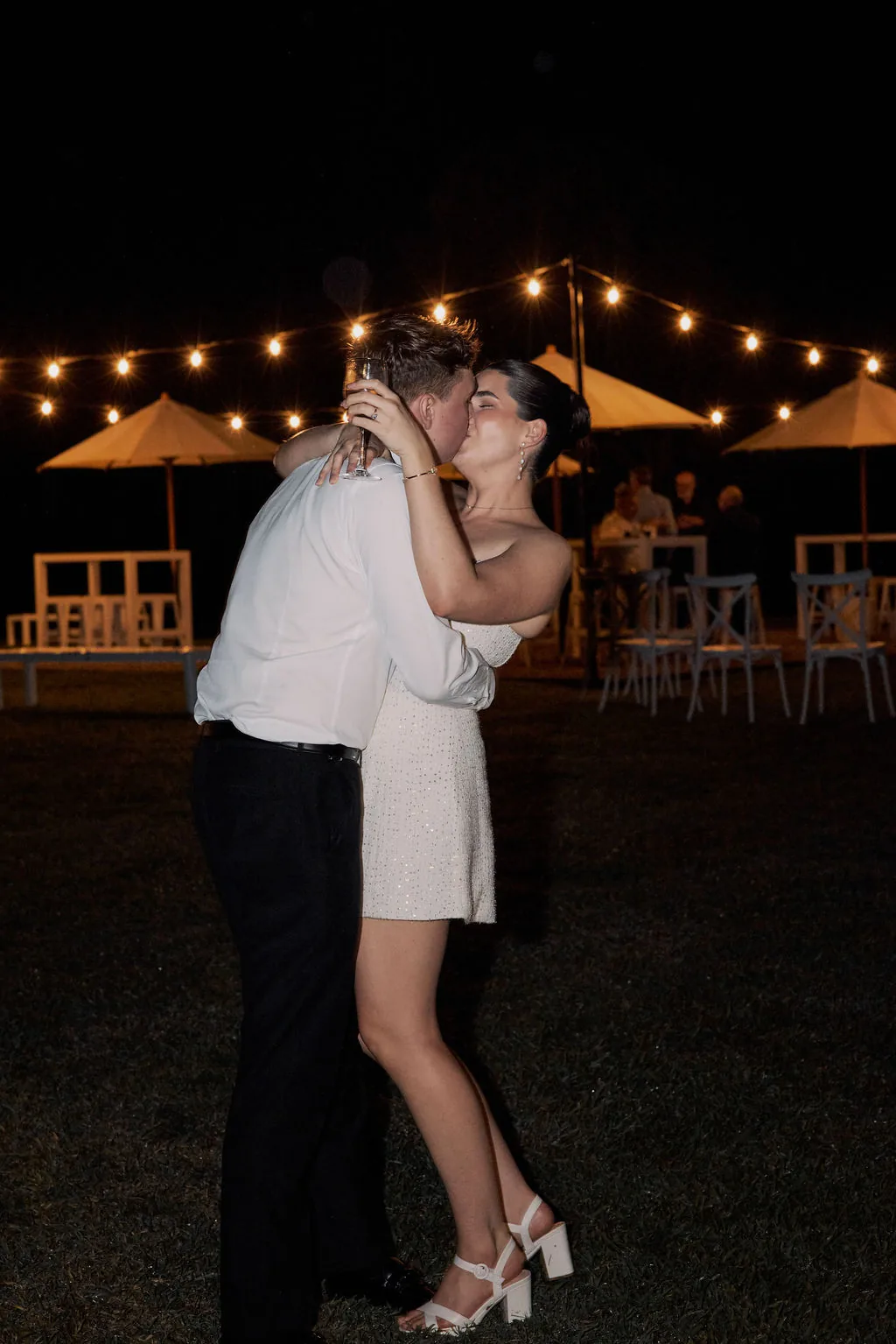 Rebecca and Benjamin sharing a kiss on the dance floor at night under festoon lights