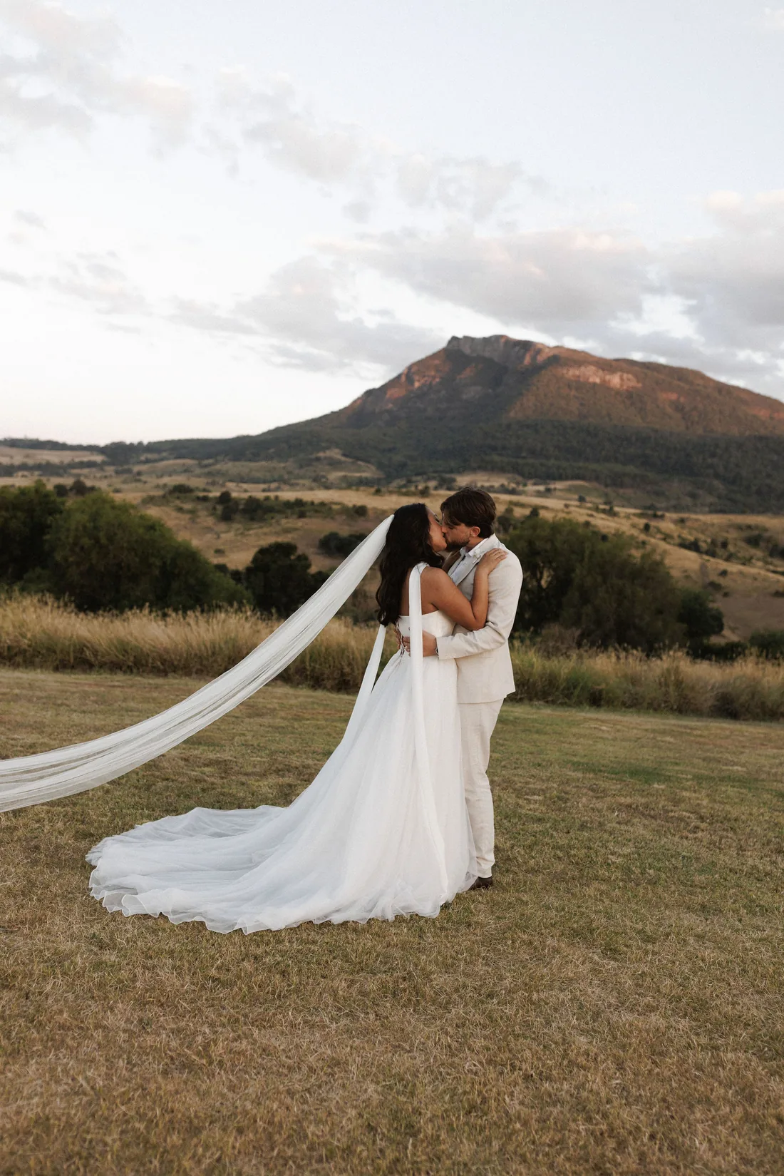 Hamish and Sarah kissing at dusk, veil trailing in the breeze, mountain silhouette behind