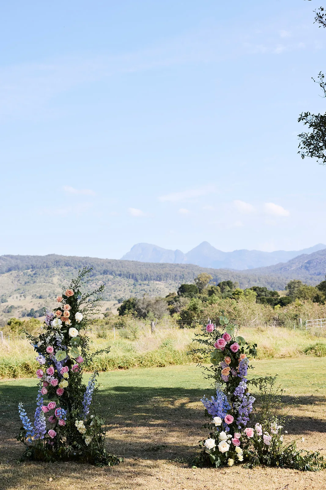 Ceremony arches wrapped in pink, lilac and white florals, framed by rolling hills and mountains at Maroon Hill Estate