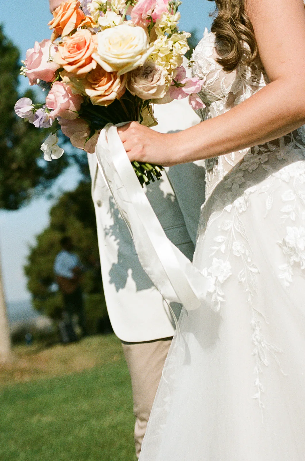 Close-up of the bridal bouquet in orange, cream and pink, with lace dress detail