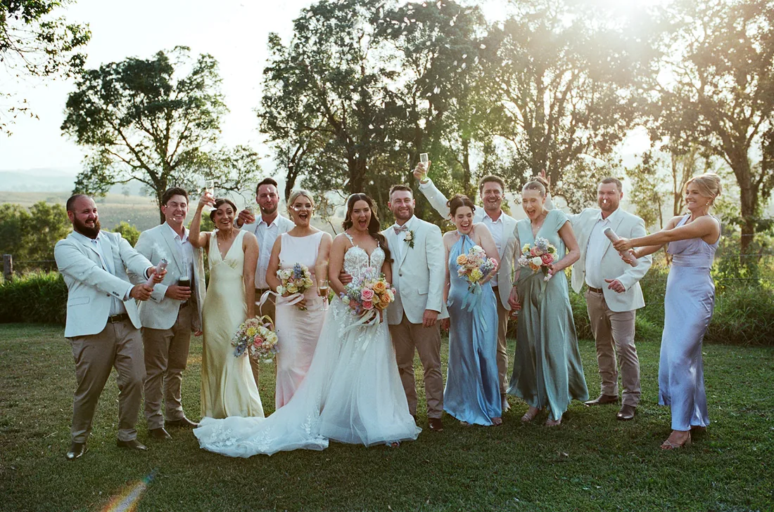 Full bridal party celebrating with raised drinks in the golden evening light