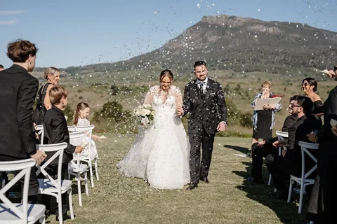 A couple walking back up the aisle through confetti, Mount Maroon behind