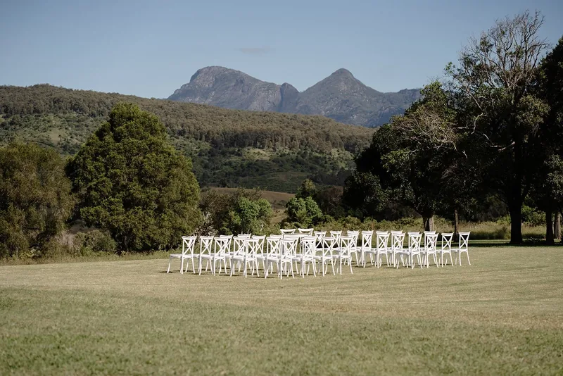 Rows of white cross-back chairs set on the lawn for a ceremony, the ranges behind