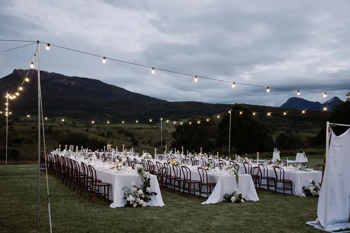 The Green set for an open-air banquet dinner beneath festoon lights, with mountains behind