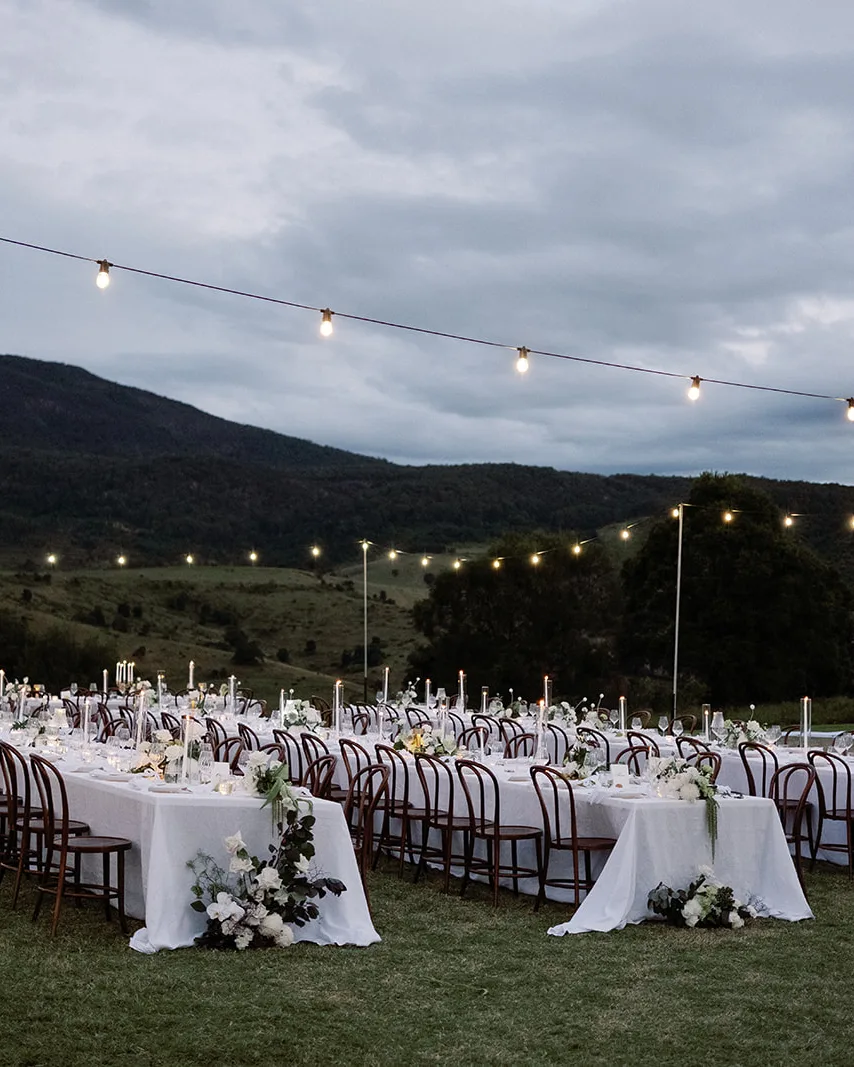 Long tables set on the lawn under festoon lights at dusk