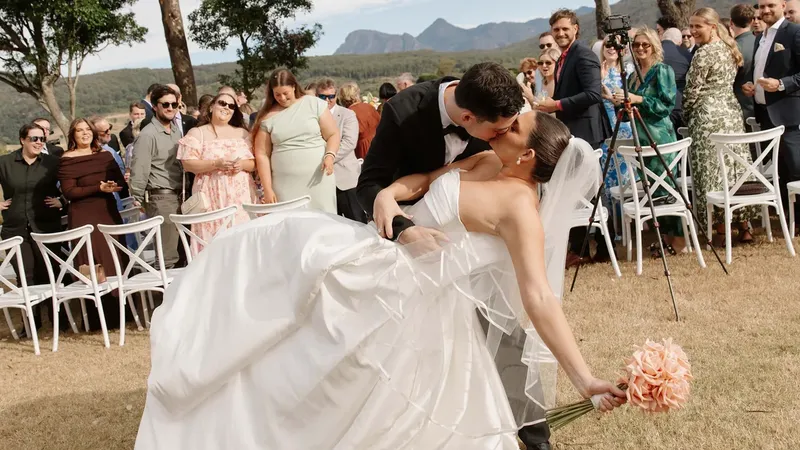Laura and Connor's first kiss as their guests cheer, Mount Maroon behind the ceremony lawn
