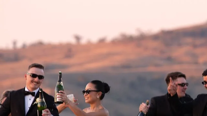 Lesley and Louis raising champagne with their wedding party at sunset, the hills glowing behind them